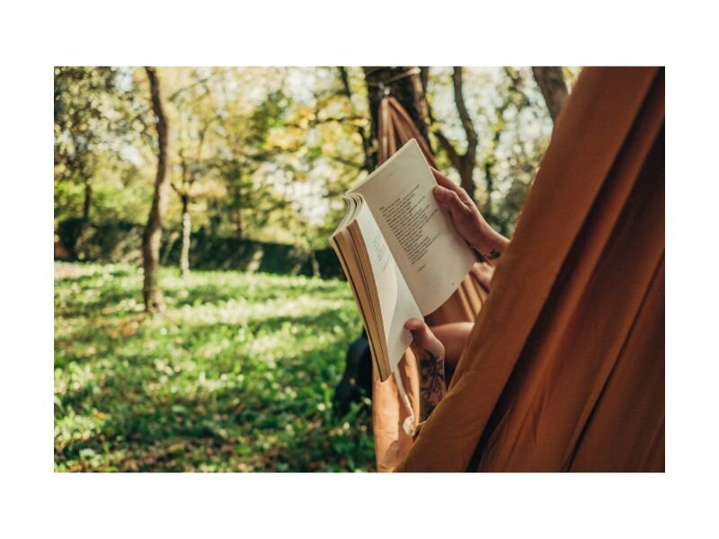 Femme lisant un livre dehors, dans son hamac, profitant d’un moment de relaxation pour équilibrer vie de famille et travail.
